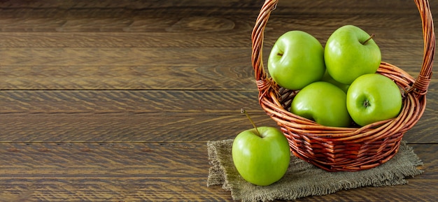 Manzanas Granny Smith orgánicas en una canasta de mimbre sobre mesa de madera. Bandera.