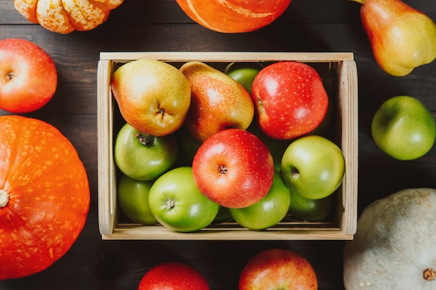 Manzanas maduras en una caja con calabazas y peras en madera oscura