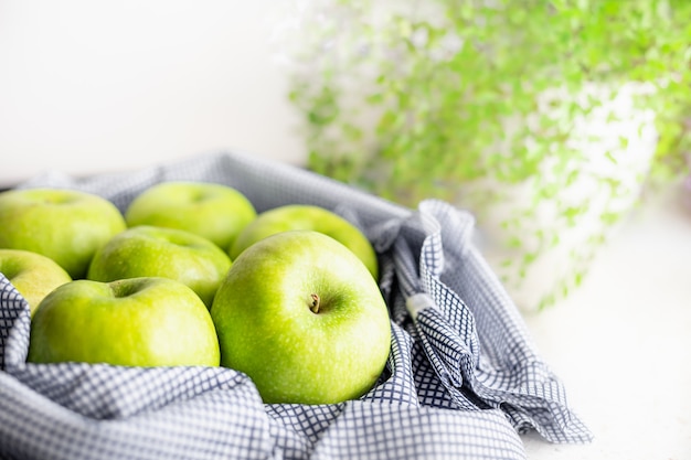 Manzanas maduras verdes sobre tela azul sobre la mesa de la cocina blanca