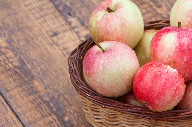 Manzanas rojas en canasta de mimbre y sobre viejas tablas de madera.