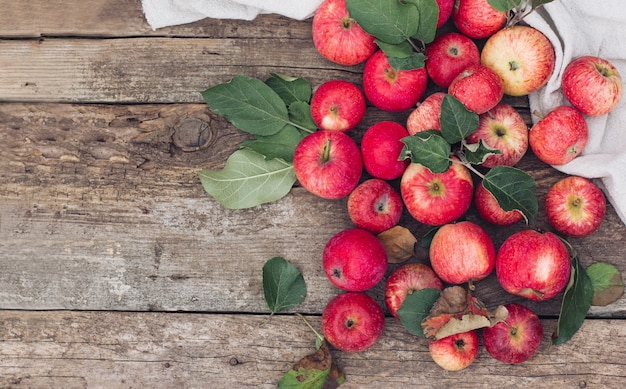 Las manzanas rojas se esparcen sobre un paño ligero sobre una mesa de madera. Estado de ánimo otoñal, vibraciones y colores otoñales, estilo de moda del otoño.