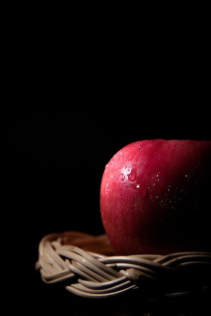 manzanas rojas frescas en una cesta con gotas de agua sobre fondo negro Hay espacio para el texto.