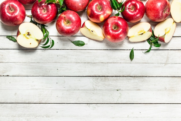 Manzanas rojas frescas con hojas. Sobre una mesa de madera blanca.