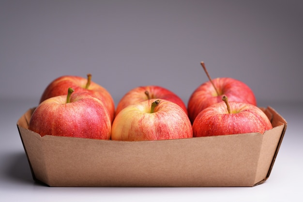 Manzanas rojas frescas en un recipiente de papel Manzanas rojas frescas en caja sobre fondo gris