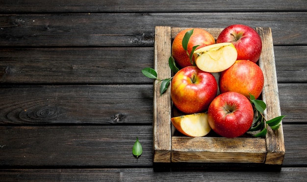 Manzanas rojas con hojas y rodajas de manzana en una caja de madera