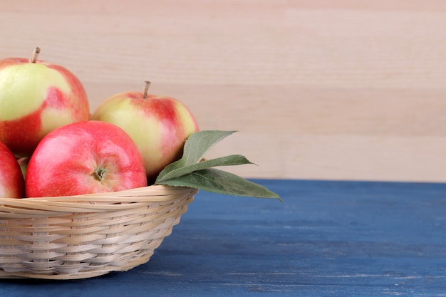 Manzanas rojas maduras frescas con hojas en una canasta sobre una mesa de madera azul y sobre un fondo de madera natural con un lugar para una inscripción