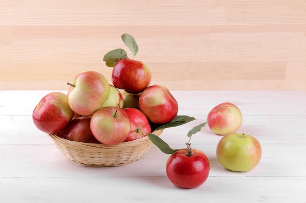 Manzanas rojas maduras frescas con hojas en una canasta sobre una mesa de madera blanca y sobre un fondo de madera natural