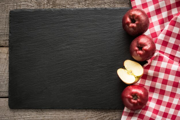 Las manzanas rojas maduras en el tablero de madera con la servilleta a cuadros roja alrededor y el espacio de la copia en pizarra negra sirven su menú.