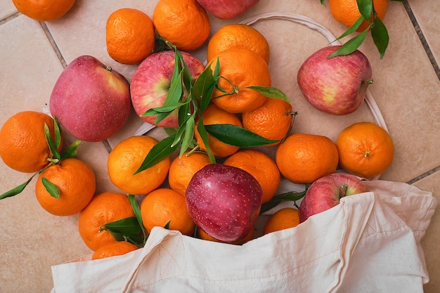 Manzanas rojas y mandarinas en una bolsa ecológica reutilizable en un piso de cerámica Entrega de frutas del mercado de agricultores alimentos saludables Vista superior de frutas jugosas