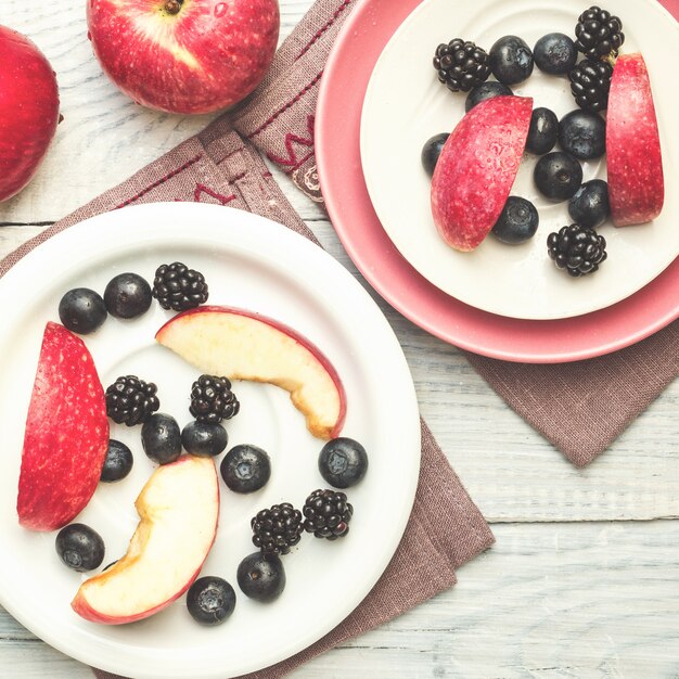 Manzanas rojas, moras y arándanos en placas sobre una mesa de madera blanca