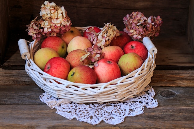 Foto manzanas rosas en una cesta blanca y hortensias de flores (de cerca)