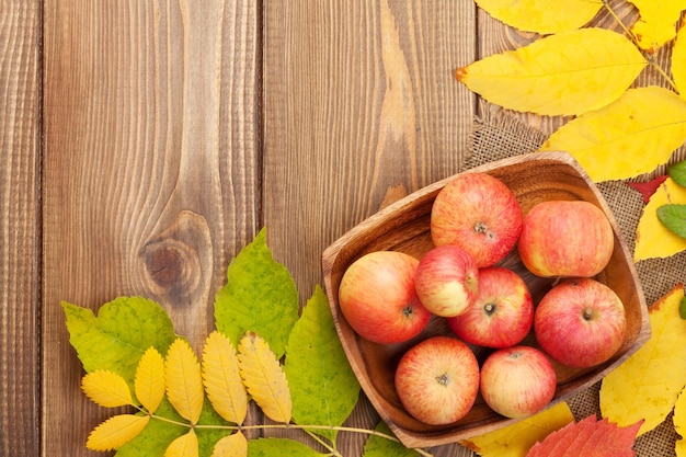Manzanas en un tazón y coloridas hojas de otoño sobre fondo de madera