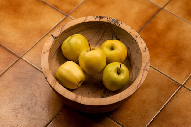 Manzanas verdeamarillas en un plato de madera sobre una superficie de baldosas de cerámica amarilla