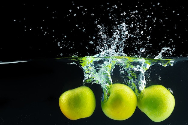 Manzanas verdes cayendo al agua con un toque contra el negro