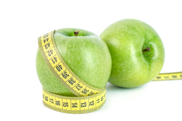 Manzanas verdes con cinta métrica sobre fondo blanco en concepto de dieta saludable.