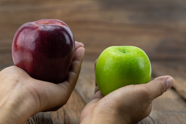 Manzanas verdes, manzanas rojas en las manos, con un fondo de madera.