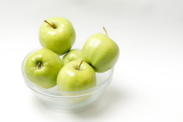 Manzanas verdes en un recipiente transparente sobre un fondo blanco.