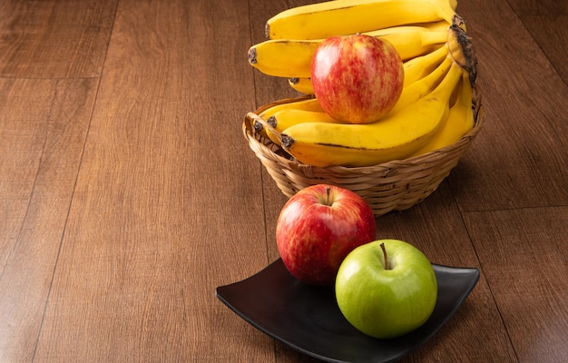 Manzanas verdes y rojas colocadas en placa negra y plátanos sobre madera