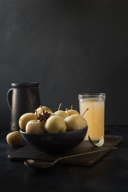 Manzanas en vinagre en un tazón y sidr de manzana en la mesa de piedra oscura.