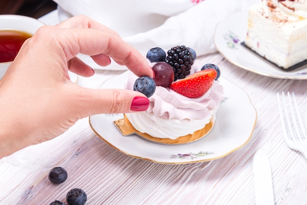 Mão agarrando um pedaço de bolo de baga decorado com frutas frescas em um fundo branco de madeira