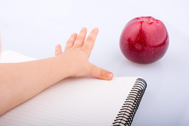 Mão alcançando uma maçã vermelha em um caderno