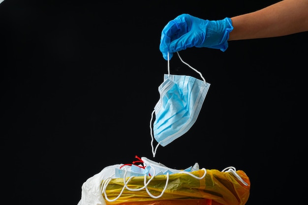 Foto mão colocando máscara cirúrgica suja usada em uma lata de lixo