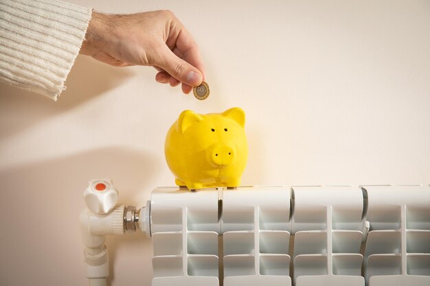 Mão colocando moedas no cofrinho no radiador de aquecimento