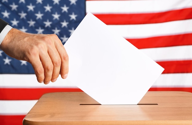 Foto mão colocando papel de votação em uma urna no fundo da bandeira americana