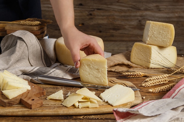Mão coloque um pedaço de queijo caseiro fresco em uma placa de madeira de perto