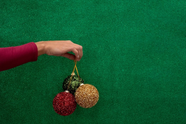 Mão com bolas de Natal vermelhas, verdes e douradas sobre um fundo verde brilhante