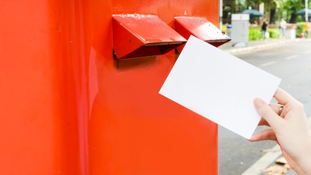 Mão com cartão postal e soltar na caixa postal de correio vermelho