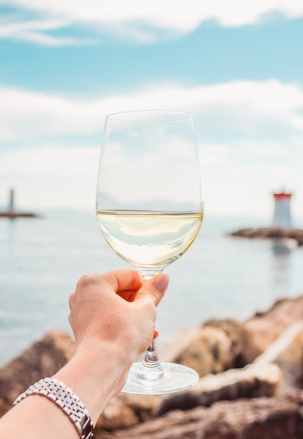 mão com copo de vinho branco em um fundo de pedras do mar e farol na França