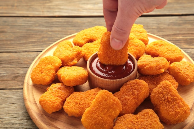 Mão com deliciosas nuggets e ketchup em fundo de madeira cinza