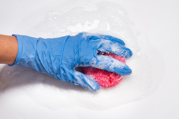 Foto mão com espuma segurando uma esponja de metal, limpando a superfície branca