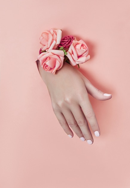 Mão com flores de papel e unhas pintadas é empurrada através de um buraco no papel