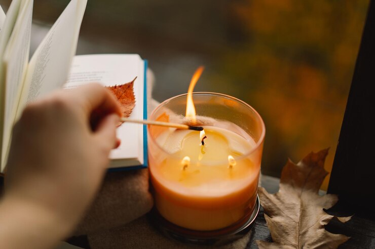Foto mão com fósforo ardente acendendo uma vela no peitoral da janela com decoração de outono