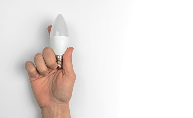 Mão com lâmpada LED em um fundo de mesa branco com foto do espaço de cópia