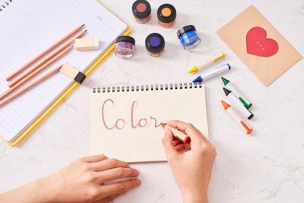 Mão com lápis de cor e folha de papel em branco na mesa branca