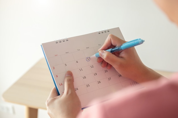 Mão com marca de caneta no dia 5 na data do calendário com círculo azul