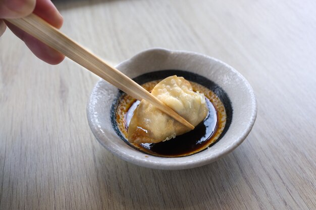 Mão com pauzinhos segurando um pedaço de gyoza frito