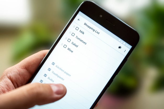 Mão com smartphone, lista de compras no telefone. lista o que comprar