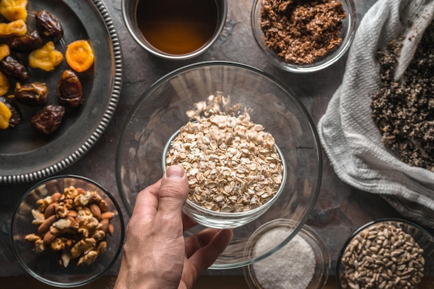 Mão com uma tigela de aveia e ingredientes para a granola