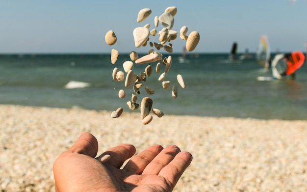 Foto mão cortada com seixos no ar na praia