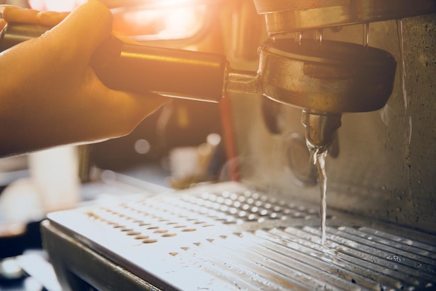 Mão cortada de barista segurando filtro porta abaixo da máquina de expresso em um café