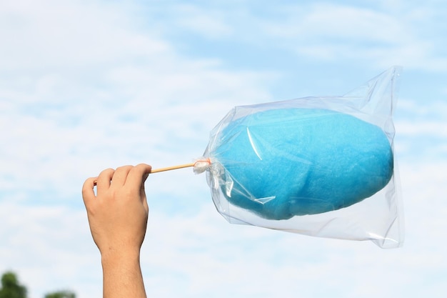 Foto mão cortada de criança segurando algodão doce azul contra o céu