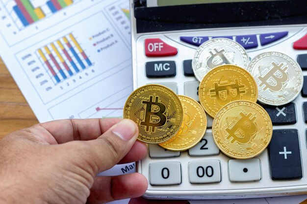 Mão cortada de homem segurando bitcoin com calculadora na mesa