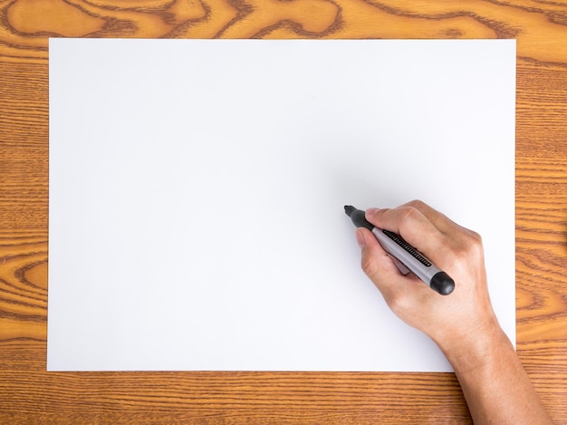 Foto mão cortada de homem segurando caneta de ponta de feltro sobre papel em branco em uma mesa de madeira