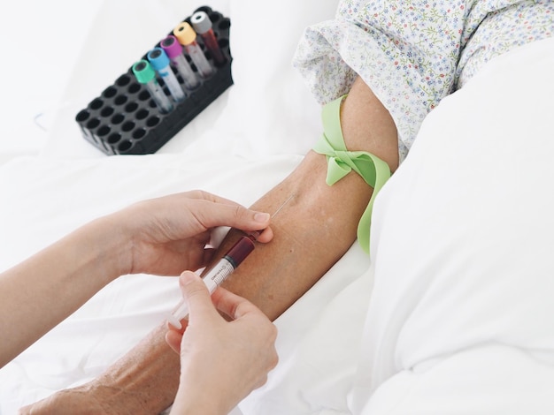 Foto mão cortada de médico segurando seringa pela mão do paciente na cama no hospital.