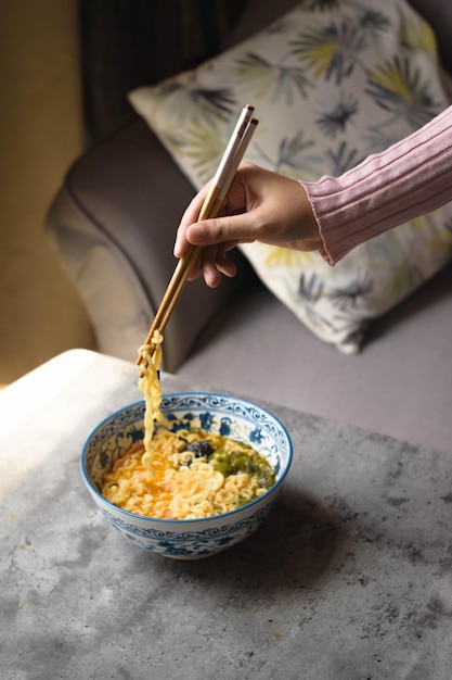 Mão cortada de mulher comendo macarrão na mesa em casa