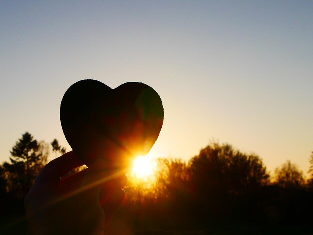 Mão cortada de mulher segurando decoração em forma de coração contra o céu durante o pôr do sol